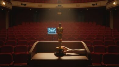 Golden Oscar statuette centered on wooden podium in empty theater with red seats, one hand on base, faint laptop glow in background.